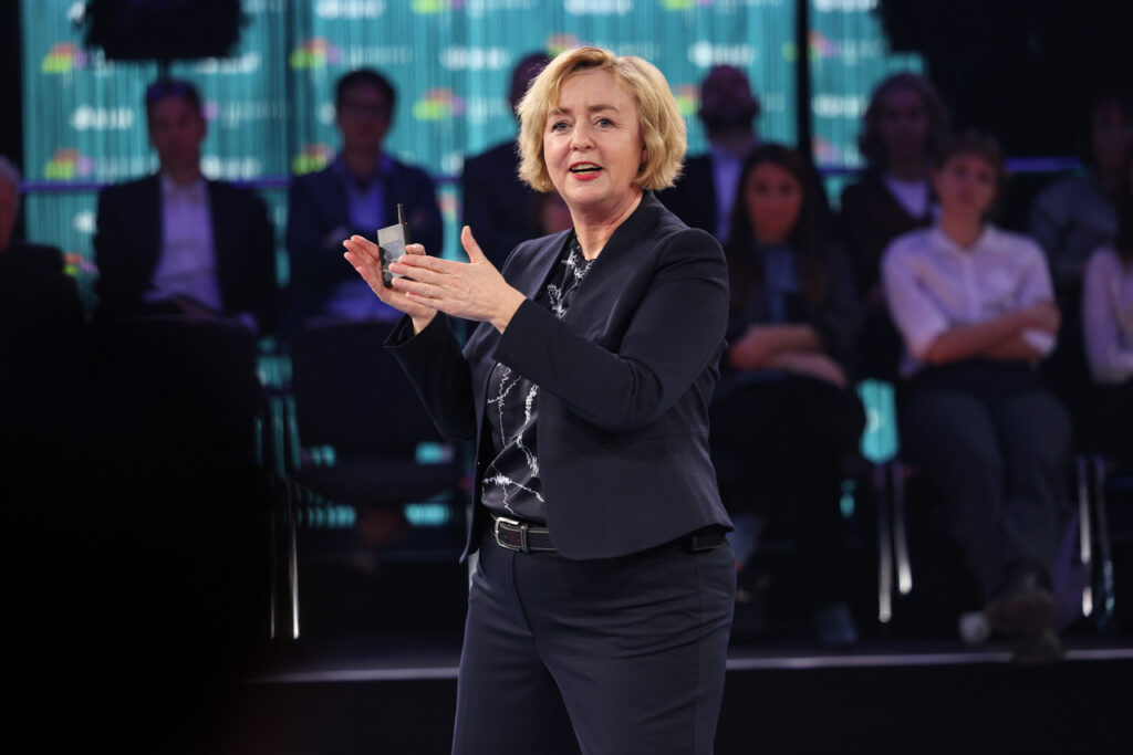 Claudia Bünte ist bei einer Keynote Präsentation vor Ort zu sehen, wie sie einen Vortrag hält und dabei gestikuliert.